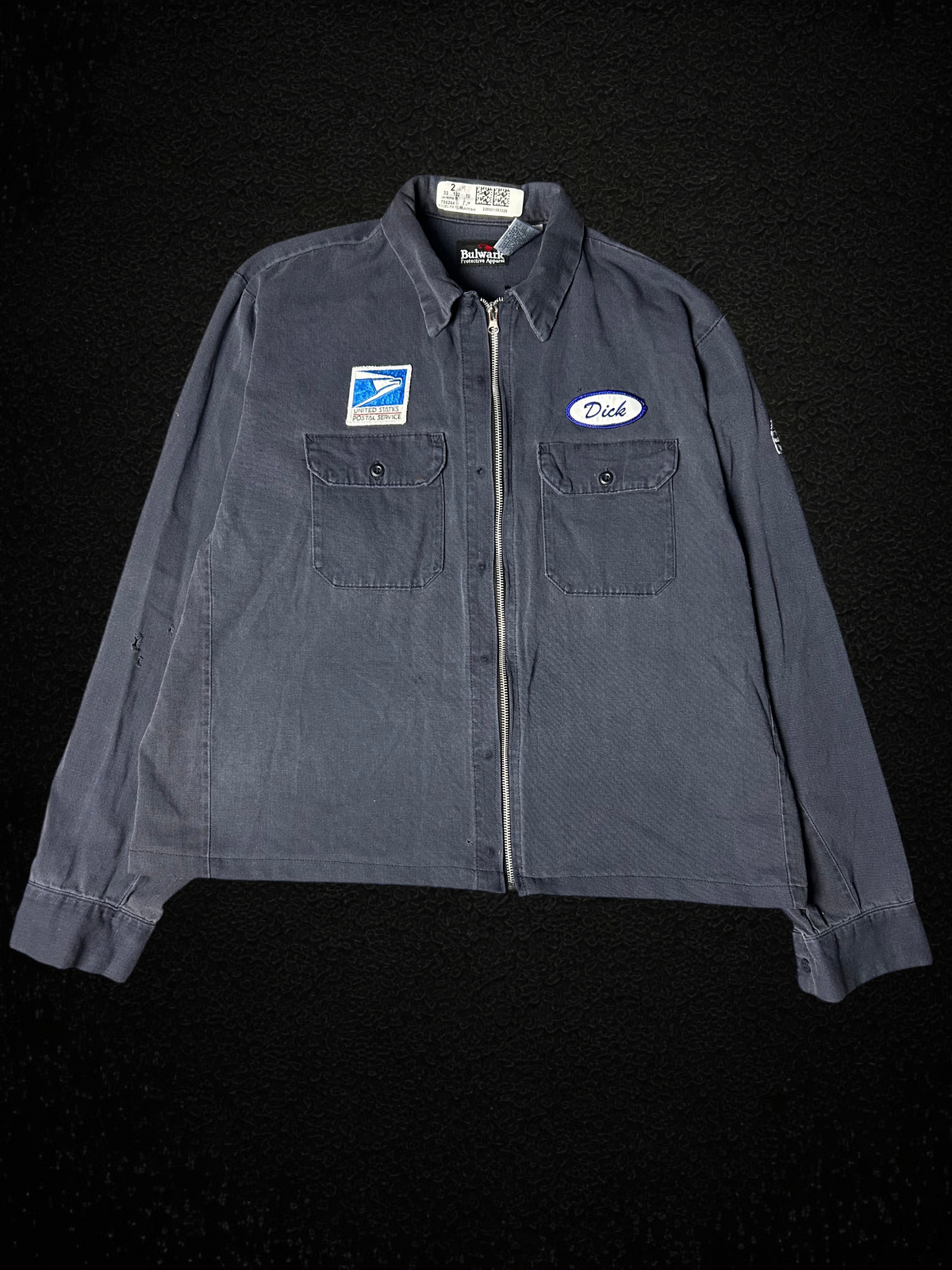 Camino’s Auto Parts vintage reworked USPS work jacket in charcoal grey with zipper closure and embroidered patches.