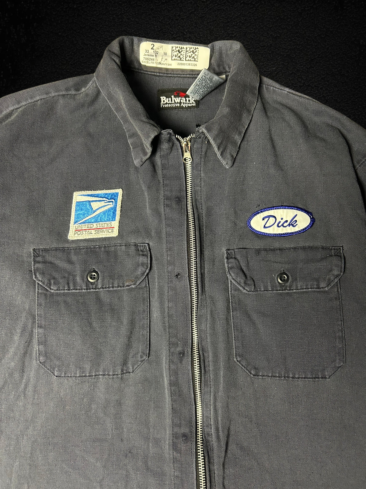 Camino’s Auto Parts vintage USPS rework jacket in grey with a front zipper, postal patch, and Dick name tag.