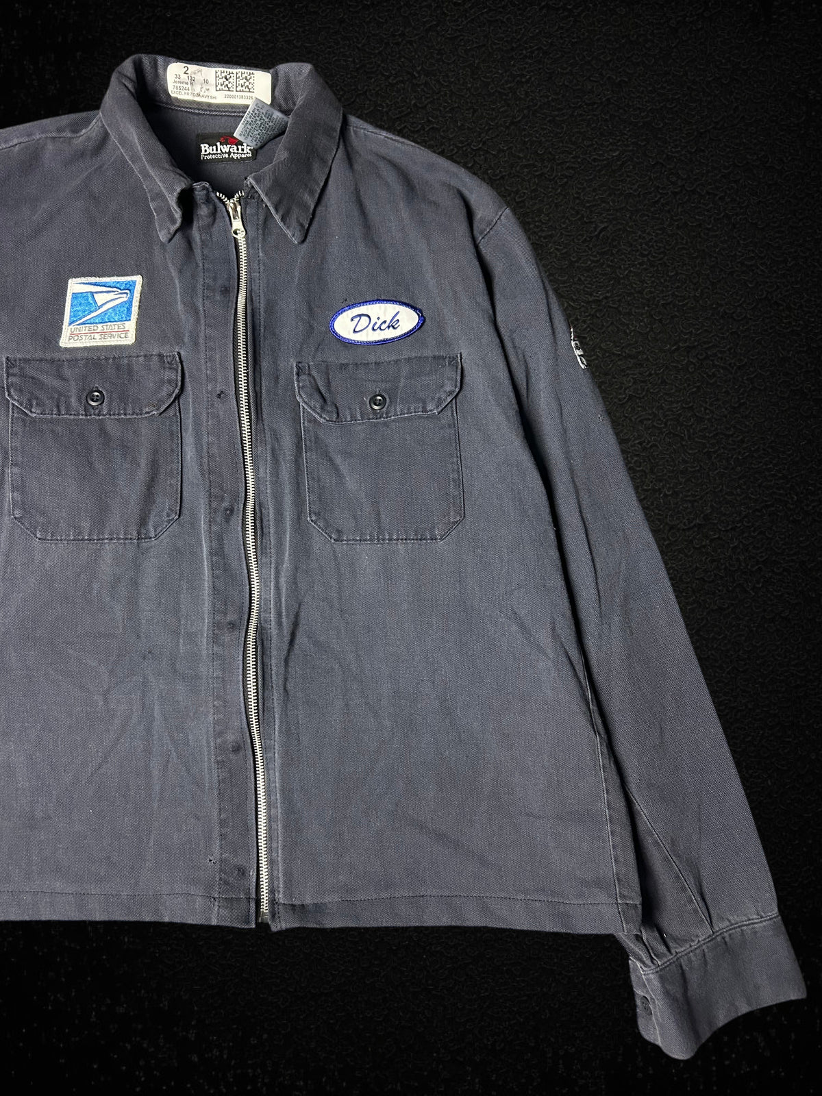 Camino’s Auto Parts vintage USPS rework jacket in grey with zipper closure, front pockets, and Dick name tag patch.